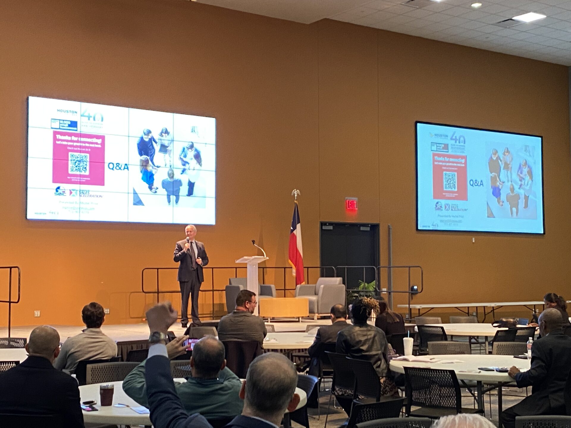 Small business owners and entrepreneurs at a conference, listening to a keynote speaker on stage next to a Texas state flag