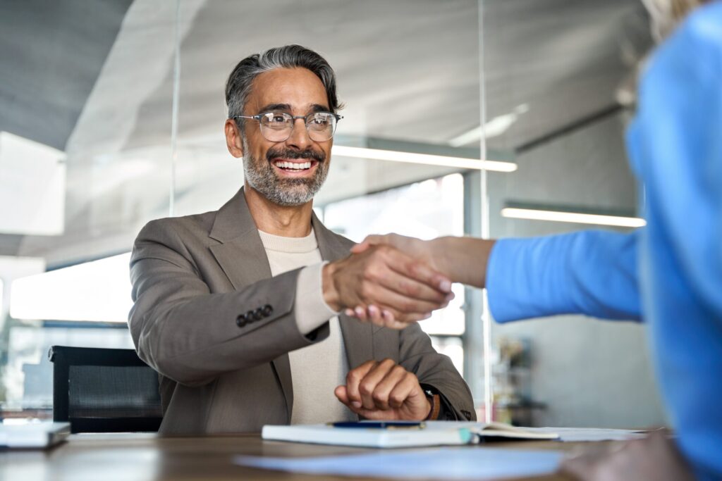 Mature smiling happy professional businessman executive, male hr recruiter or bank manager hiring recruit at job interview onboarding corporate office meeting. Handshake with new client concept.