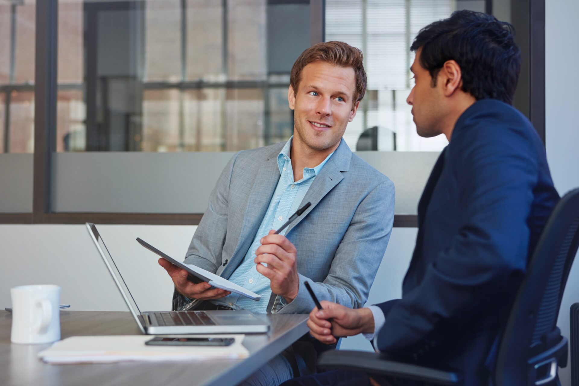 Laptop, notes and man in office with advisor, business plan and collaboration for proposal ideas. Advice, consultant and businessman in meeting for project management, teamwork or online research