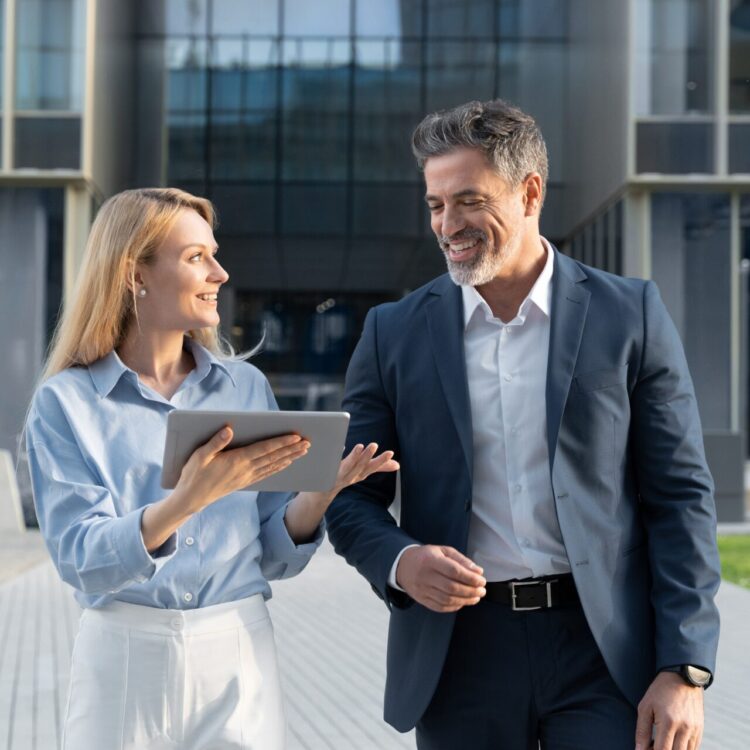 Mature 40s years old man, young adult woman walking, discussing project on digital pc tablet computer. Successful middle aged latin hispanic businessman, businesswoman work together on business plan