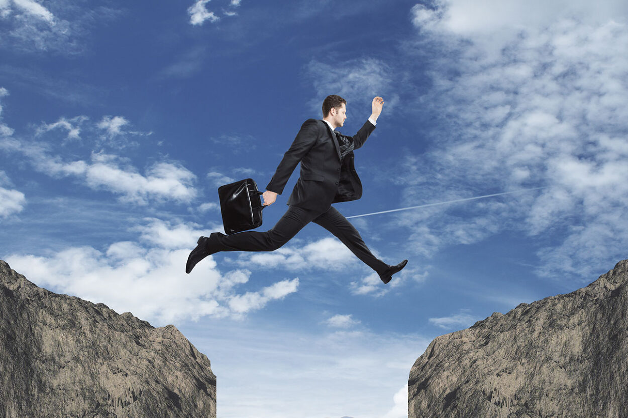Business man jumping from one cliff to another